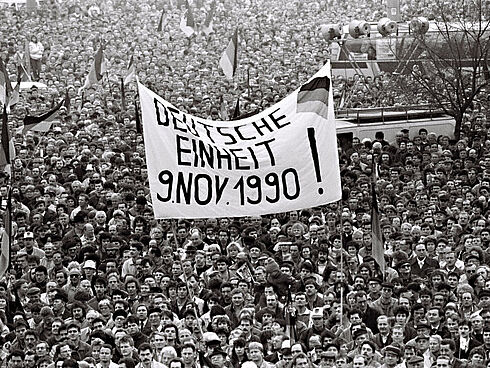 Fotografie einer Wahlkundgebung. Die Menschen halten Plakate und Deutschlandfahnen in die Höhe