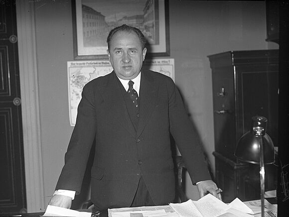 Schwarz-Weiß-Foto von Walther Funk, der an einem Schreibtisch steht und in die Kamera blickt.