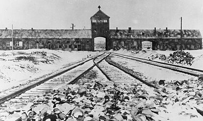 Blick auf das Eingangstor von Auschwitz. Im Vordergrund sind Schienen zu sehen.