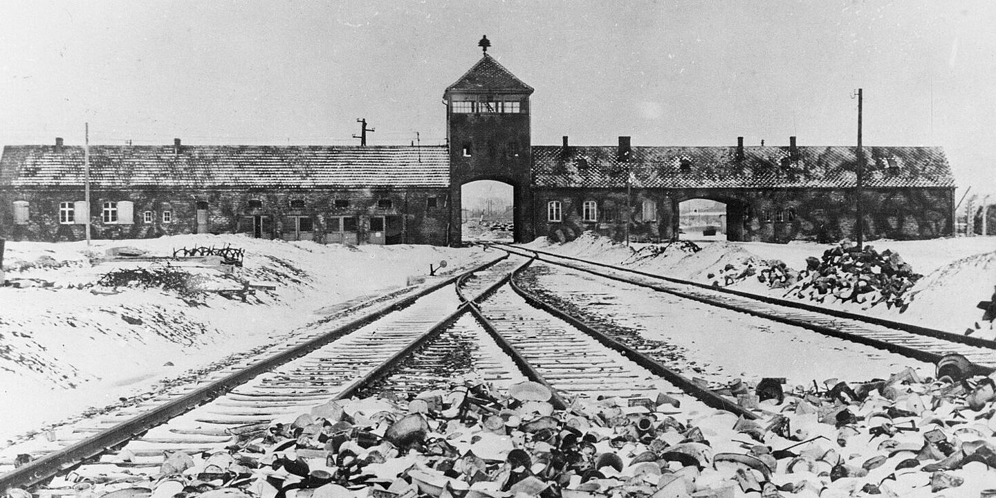 Blick auf das Eingangstor von Auschwitz. Im Vordergrund sind Schienen zu sehen., Quelle:
            BArch, B 285 Bild-04413 / Mucha, Stanislaw
