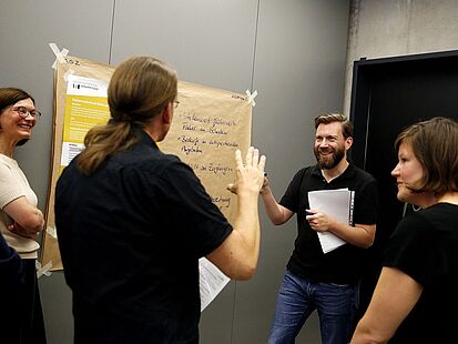 Vier Personen stehen vor einem Plakat und sprechen miteinander.