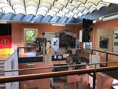 Blick von oben in den Ausstellungsraum in Rastatt. Zu sehen sind mehrere Informationstafeln und eine schwarz-rot-goldene Fahne.