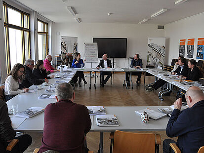 Männer und Frauen sitzen an Tischen und sprechen miteinander.