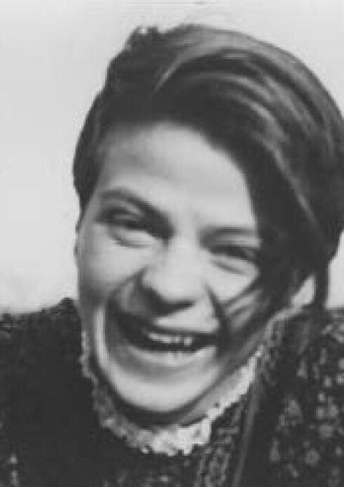 Portrait-Aufnahme von einer lachenden Sophie Scholl mit kurzen Haaren und einer Bluse mit Blumenmuster in der Natur.