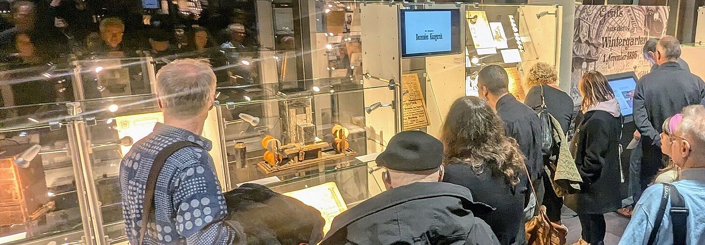 Mehrere Personen schauen sich beleuchtete Vitrinen an, die mit Dokumenten gefüllt sind.