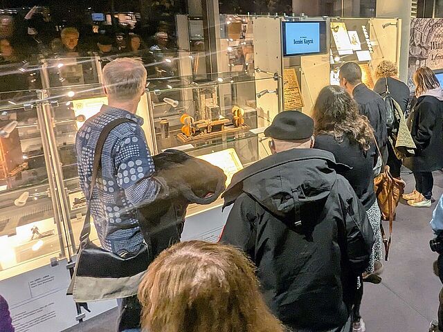 Mehrere Personen schauen sich beleuchtete Vitrinen an, die mit Dokumenten gefüllt sind.