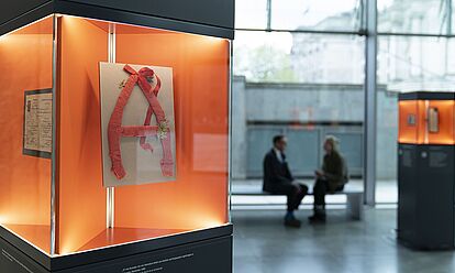 Eine Glasvitrine, in der sich ein aus Alufolie und Krepppapier gebasteltes 'A' befindet.