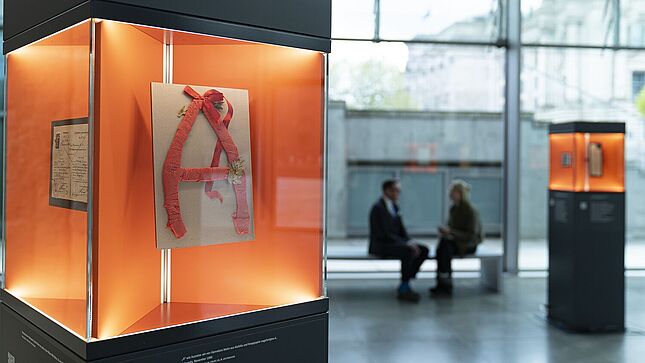 Eine Glasvitrine, in der sich ein aus Alufolie und Krepppapier gebasteltes 'A' befindet.