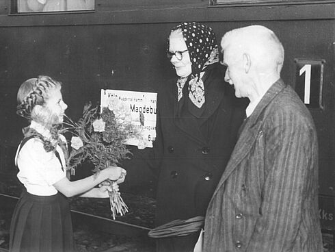 Mädchen in Pionieruniform überreicht einen Blumenstrauß an die ersten Gäste aus dem Westen 1954