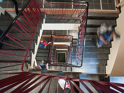 Treppenhaus, von oben fotografiert, in dem Menschen nach unten laufen.