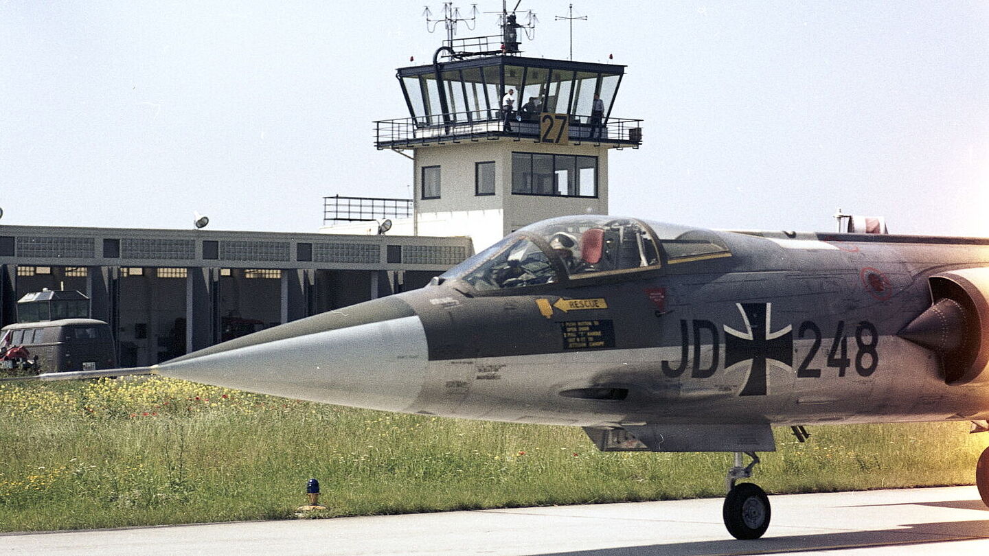 Ein Jagdflugzeug F-104G „Starfighter“ des Jagdgeschwaders 74 „Mölders“ steht auf einer Rollbahn. Im Hintergrund ist ein Tower zu sehen., Quelle:
            BArch,&nbsp;B 145 Bild-F027409-0011 / Berretty&nbsp;