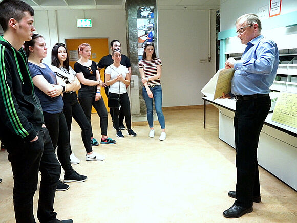 Ein Mitarbeiter des Stasi-Unterlagen-Archivs steht vor einem Karteiumlaufschrank und erläutert anhand einer Karteikarte die Datenspeicherung durch die Stasi. 