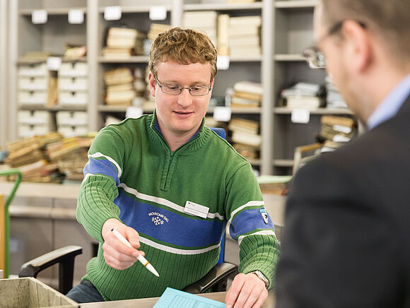 Ein Mitarbeiter bei der Erläuterung und Aushändigung eines Benutzungsantrages an einen Benutzer.
