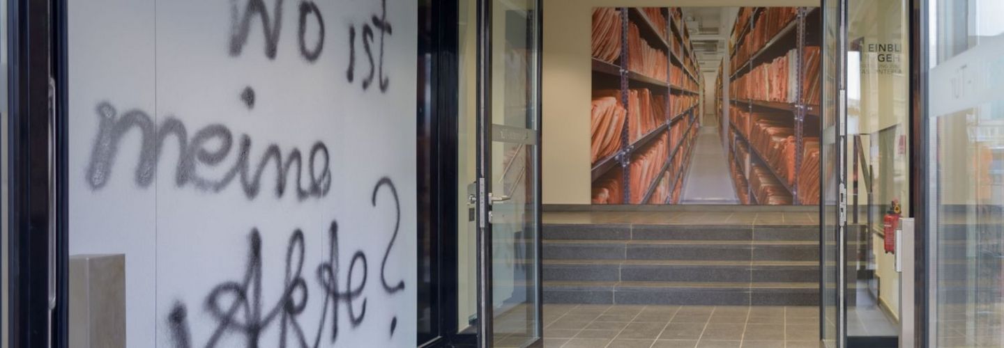 Der Eingangsbereich der Ausstellung 'Einblick ins Geheime'. Zwei Türen sind geöffnet, an der linken Seite steht an der Wand geschrieben: 'Wo ist meine Akte?'.