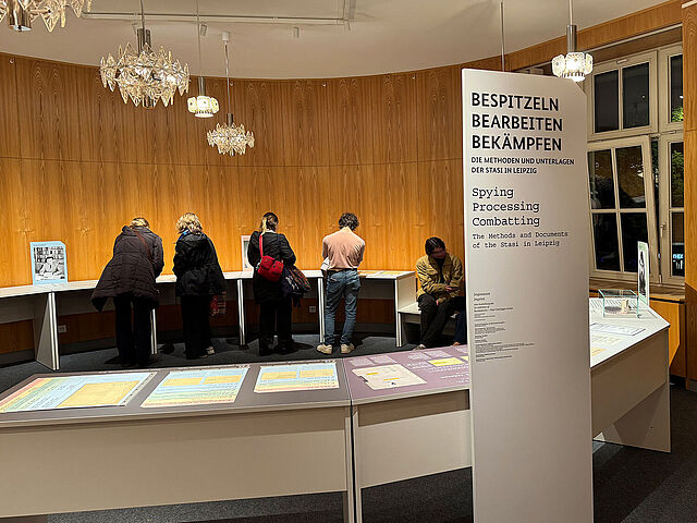 Menschen in einem holzgetäfelten Raum mit Ausstellungstischen