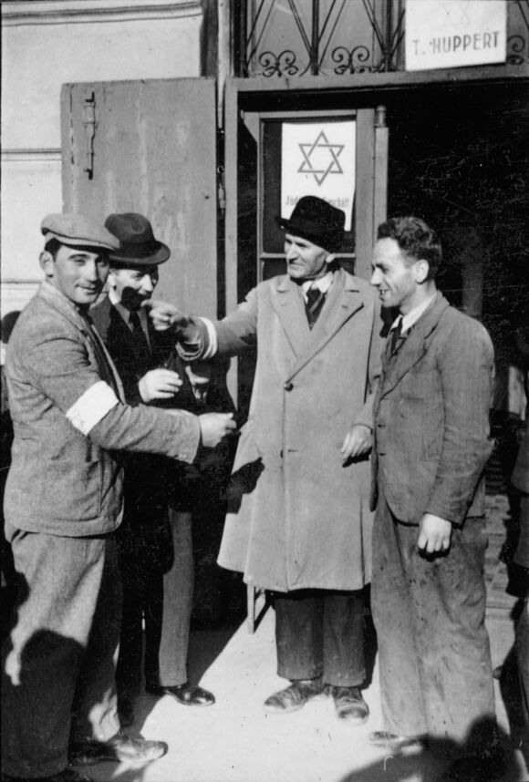 Jüdische Männer, z.T. mit Judenstern auf Armbinden, vor einem Geschäft mit dem Schild „Jüdisches Geschäft“, Krakau 1940.