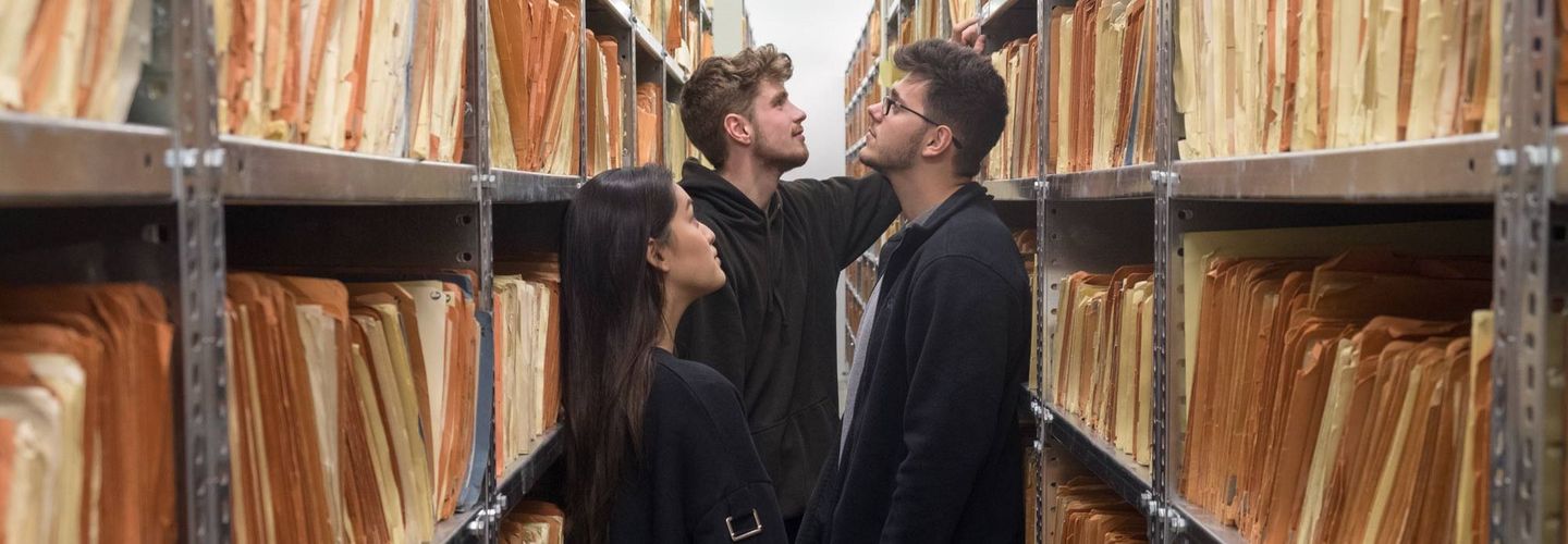 Eine Schülerin und zwei Schüler stehen in einen Magazinraum in „Haus 9“