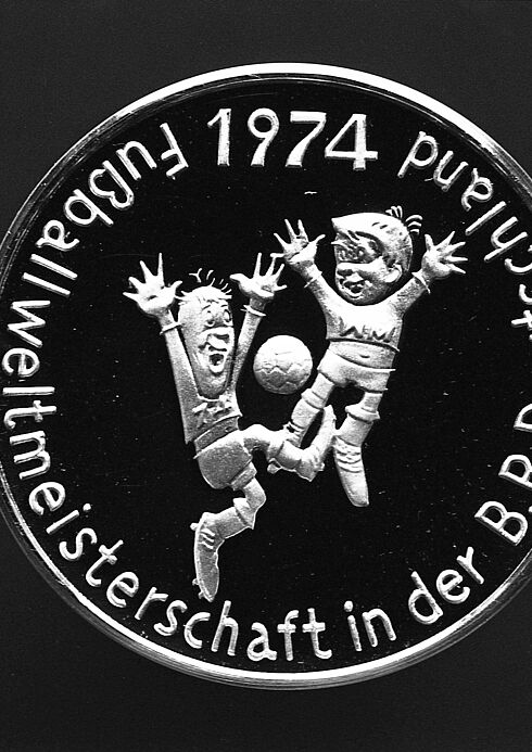 Gedenkmünze Auf der Münze sind zwei fußballspielende Figuren zu sehen. Am Rande ist die Inschrift "Fußballweltmeisterschaft in der B.R. Deutschland 1974" zu lesen.
