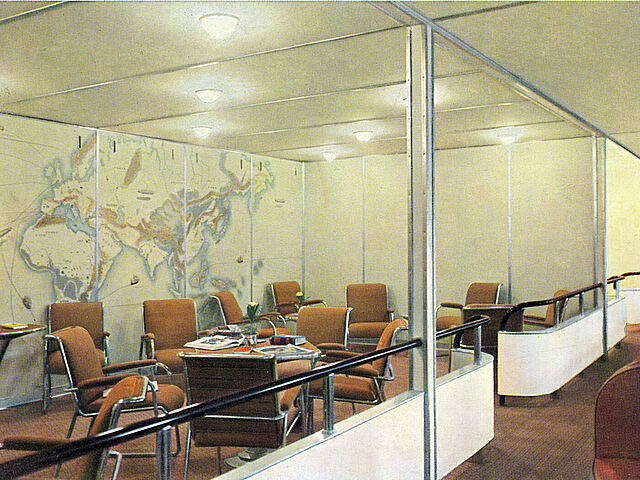 Blick in den leeren Gesellschaftsraum des Luftschiffs LZ 129 „Hindenburg“. Zu sehen sind mehrere Tische und Stühle.