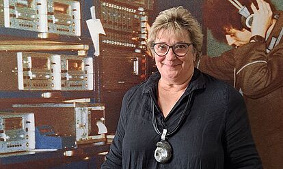 Katri Jurichs steht vor einer Fotografie eines Stasi-Mitarbeiters mit Kopfhörern.