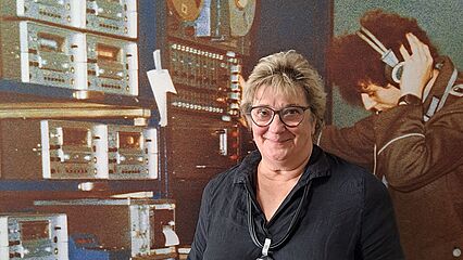 Katri Jurichs steht vor einer Fotografie eines Stasi-Mitarbeiters mit Kopfhörern.