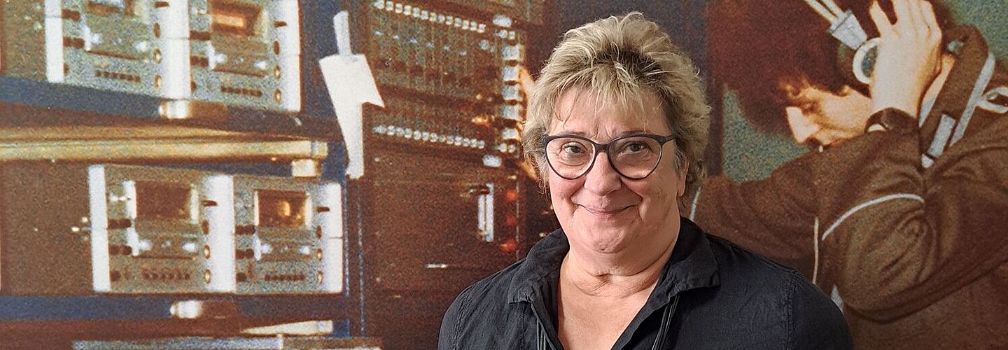 Katri Jurichs steht vor einer Fotografie eines Stasi-Mitarbeiters mit Kopfhörern.