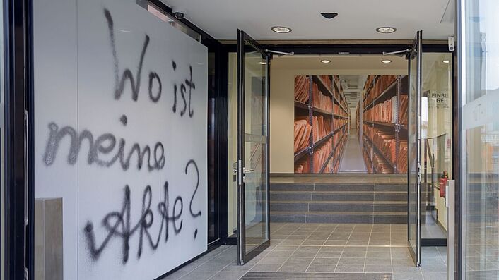 Das Bild zeigt den Eingangsbereich zur Ausstellung 'Einblick ins Geheime'. Auf einer Wand auf der linken Seite ist folgender Schriftzug zu lesen: 'Wo ist meine Akte?'