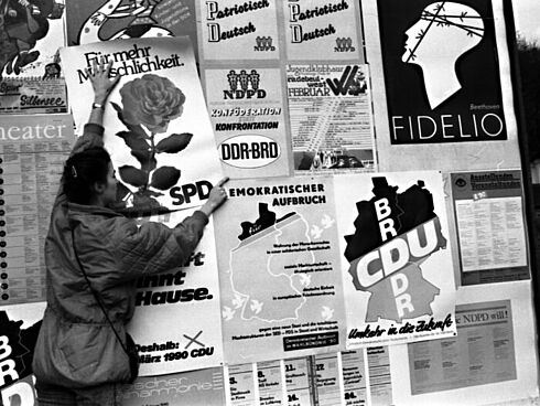 Fotografie einer DDR-Bürgerin, welche ein Wahlplakat aufhängt.
