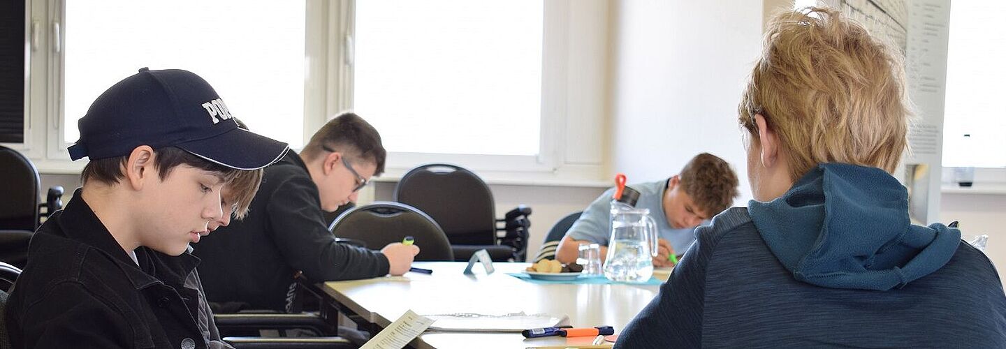 Vier Jungen sitzen an einem Tisch und beschäftigen sich mit einem Aufgabenblatt