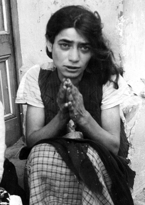 Schwarz-Weiß-Foto mit einer jungen Frau, die mit betender Handgeste vor einem Hauseingang sitzt