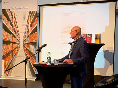 Der Zeitzeuge Lothar Rochau steht an einem Tisch und liest aus seinem Buch "Marathon mit Mauern"