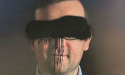 Das Bild zeigt ein beschmiertes Wahlplakat. Auf diesem ist ein Mann abgebildet, dessen Augen mit schwarzer Farbe übersprüht wurden.