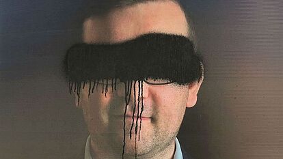 Das Bild zeigt ein beschmiertes Wahlplakat. Auf diesem ist ein Mann abgebildet, dessen Augen mit schwarzer Farbe übersprüht wurden.