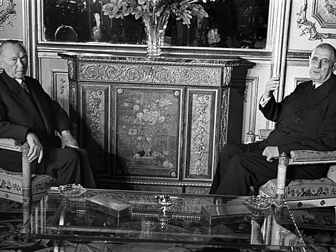Adenauer und de Gaulle sitzen sich auf edlen Polsterstühlen in einem barock eingerichteten Raum gegenüber und blicken in die Kamera.