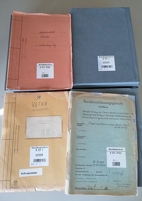 Foto der Akten zum 1. Rundfunk-Urteil des Bundesverfassungsgerichts, 1961 vier Papierakten, in zwei Reihen à zwei Mappen angeordnet, zum Teil mit handschriftlicher Beschriftung und Bundesarchiv-Signaturaufklebern versehen