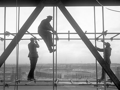 Arbeiter auf einem Gerüst am Glockenturm. Im Hintergrund: Das Olympiastadion