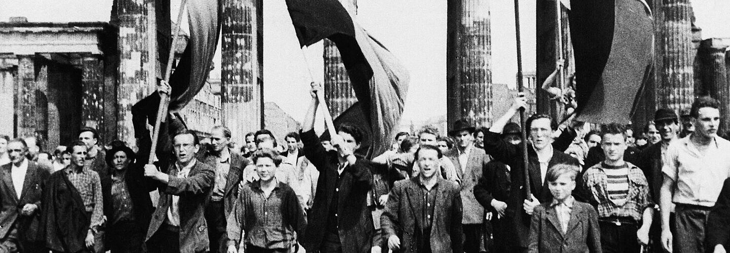 Demonstranten (mit Fahnen) gehen durch das Brandenburger Tor, 1953.