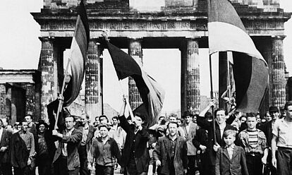 Demonstranten (mit Fahnen) gehen durch das Brandenburger Tor, 1953.