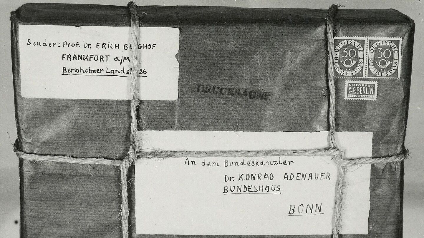 Aufgeklebtes Schwarz-Weiß-Foto eines mit Band verschnürten Pakets mit handgeschriebener Absender- und Empfängeradresse auf Etiketten, Briefmarken und „Drucksache“-Stempel; an einem darunter angelegten Zollstock ist das Maß ablesbar., Quelle:
            BArch, B 106/15789, Image 1133 (Ausschnitt)
