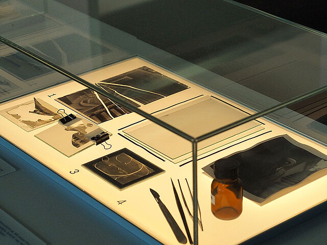 Glasvitrine mit historischen fotografischen Materialien, darunter auch ein zerbrochenes Glasnegativ