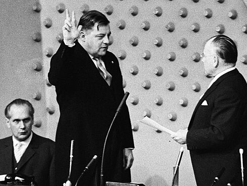 Franz Josef Strauß bei der Vereidigung zum Bundesverteidigungsminister 1961 Das Schwarz-Weiß-Foto wurde am 14. November 1961 vom Fotografen Egon Steiner aufgenommen. Festgehalten wurde die Vereidigung von Franz Josef Strauß zum Verteidigungsminister. Strauß steht mit erhobener Hand und drei gestreckten Fingern gegenüber dem Präsidenten des Deutschen Bundestages, Eugen Gerstenmaier. Dieser hält ein Blatt Papier in der Hand. Im Hintergrund sitzt ein weiterer Herr im Anzug und verfolgt das Geschehen.