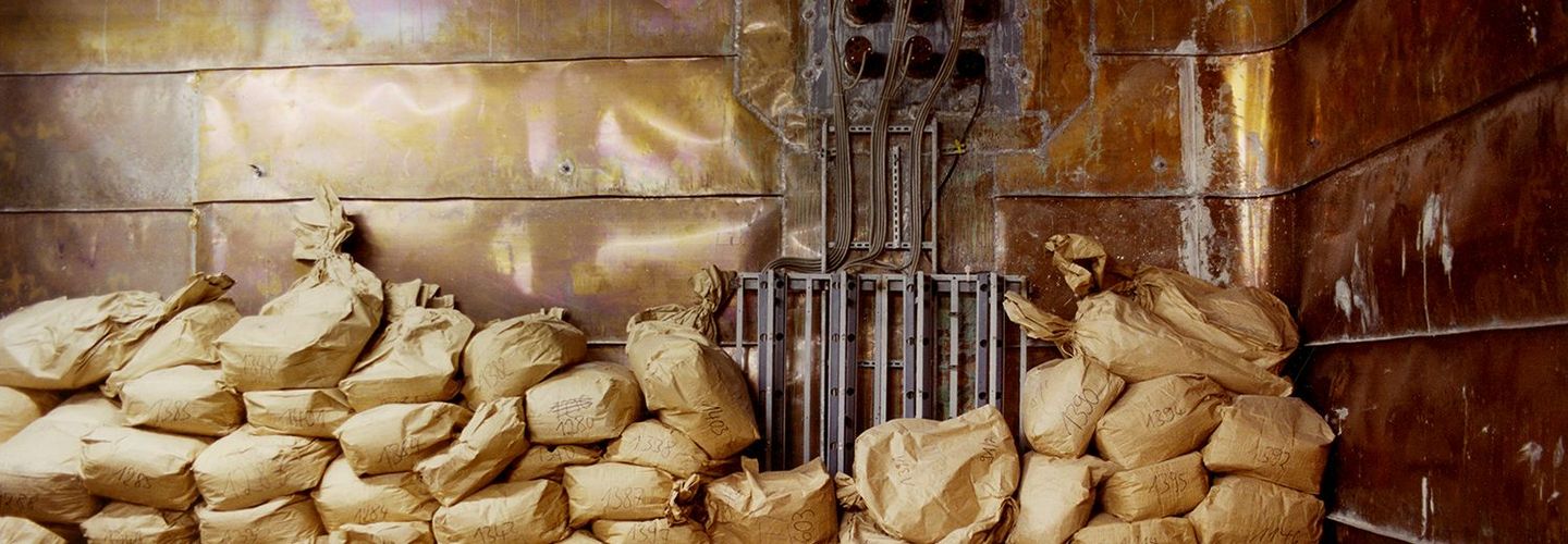 Das Bild zeigt eine Stapel mit Papiersäcken in einem mit Kupferplatten verkleideten Raum.