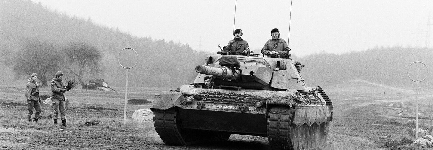 Frontansicht eines Kampfpanzers Leopard 1 in Fahrt auf einem Übungsgelände der Bundeswehr. Aus einer Turmlucke schaut Bundeskanzler Helmut Kohl.