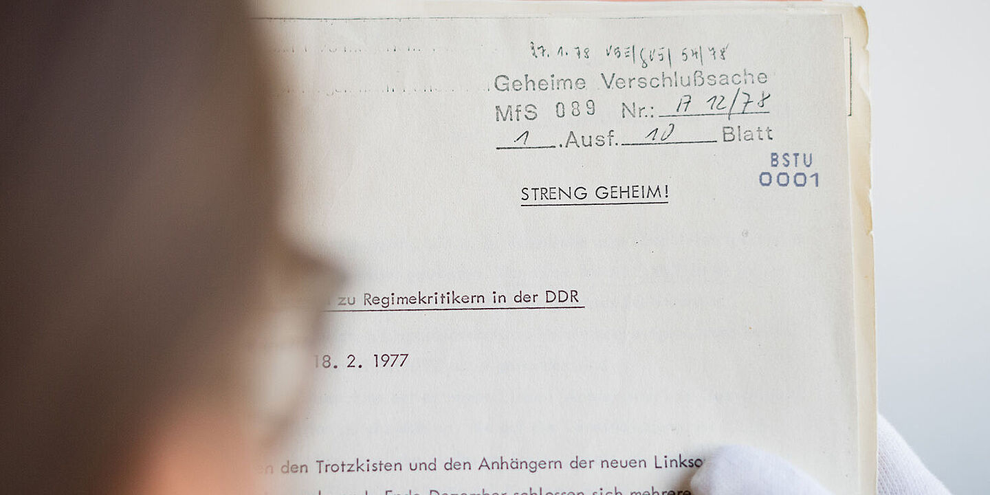 Das Bild zeigt eine Person, die eine geöffnete Akte in den Händen hält und darin liest., Quelle:
            BStU / Mulders