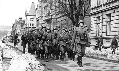 Eine Kolonne deutscher Soldaten marschiert durch eine verschneite Stadt.