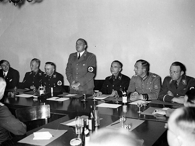 Erste Sitzung des Polizeirechtsausschusses in der Akademie für Deutsches Recht, 12. Oktober 1936 Erste Sitzung des Polizeirechtsausschusses in der Akademie für Deutsches Recht; Hans Frank bei der Begrüßung der Teilnehmer, (v.l.) Wilhelm Stuckart, Reinhard Heydrich, Heinrich Himmler, Hans Frank, Werner Best, Kurt Daluege und Wolf Heinrich Graf von Helldorf, 12. Oktober 1936