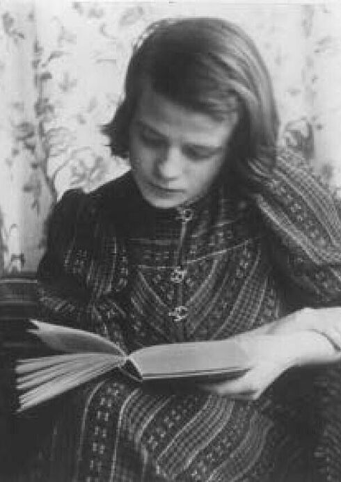 Sohpie Scholl sitzt in einem Sessel über ein Buch gebäugt. Ihre Haare trägt sie in ihrem characteristischen Bob. Sie trägt ein gemusterte langes Kleid.