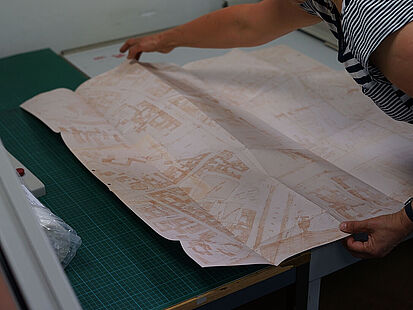 Beispielakten Eine Mitarbeiterin breitet das Replikat eines Stadtplans aus.