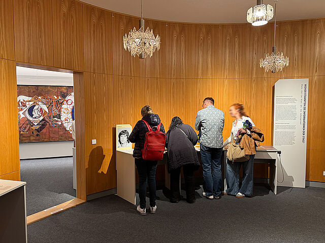 Menschen in einem holzgetäfelten Raum mit Ausstellungstischen