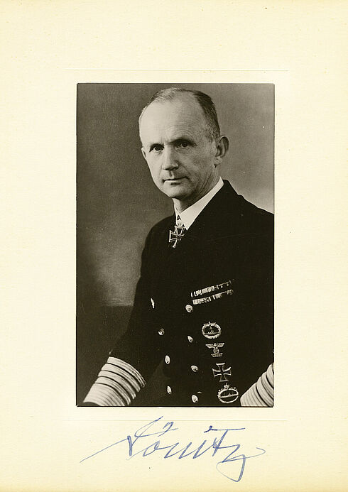Auf Papier geklebte Schwarz-Weiß-Porträtaufnahme eines Mannes in mit zahlreichen Orden geschmückter Uniform; händische Unterschrift unter dem Bild.